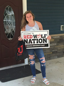 Student holding a sign that says Welcome to Red Wolf Nation and a black IU bag
