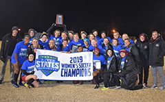 Group shot of the 2019 Women's Soccer Champions, dressed in blue and holding a banner declaring them champions