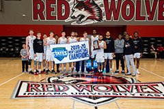 Men's basketball team in the IU East auditorium by the Red Wolves logo, holding a banner that says 2019-20 Mens Basketball Champions