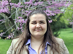 Tatyana Whited smiling, wearing a lavender blouse and neutral colored jacket, outside in front of a tree with pink blossoms