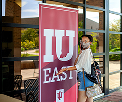 Student wearing face mask, standing by an IU East sign outside