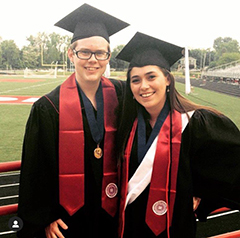O'Brien and Eversole smiling in their graduation cap, gown, and stoles in front of the university football field