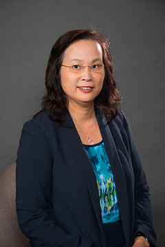 Oi Lin Cheung, smiling at camera in front of neutral background