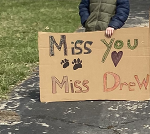 Message written on cardboard that says Miss you Miss Drew, with a drawing of a heart and paw prints.