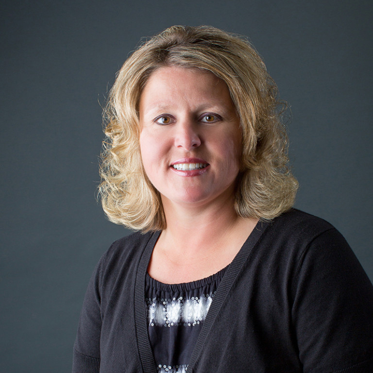 Paula Baumann smiling in front of a cool gray background.