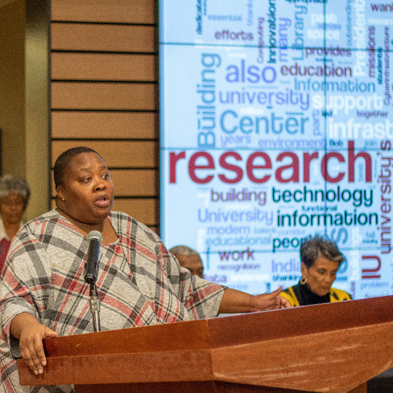 Yemi Mahoney speaks at podium with word cloud screen behind her