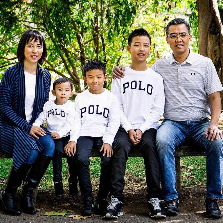 Noriko Kuwahara sitting with her three sons and husband on a bench in nature