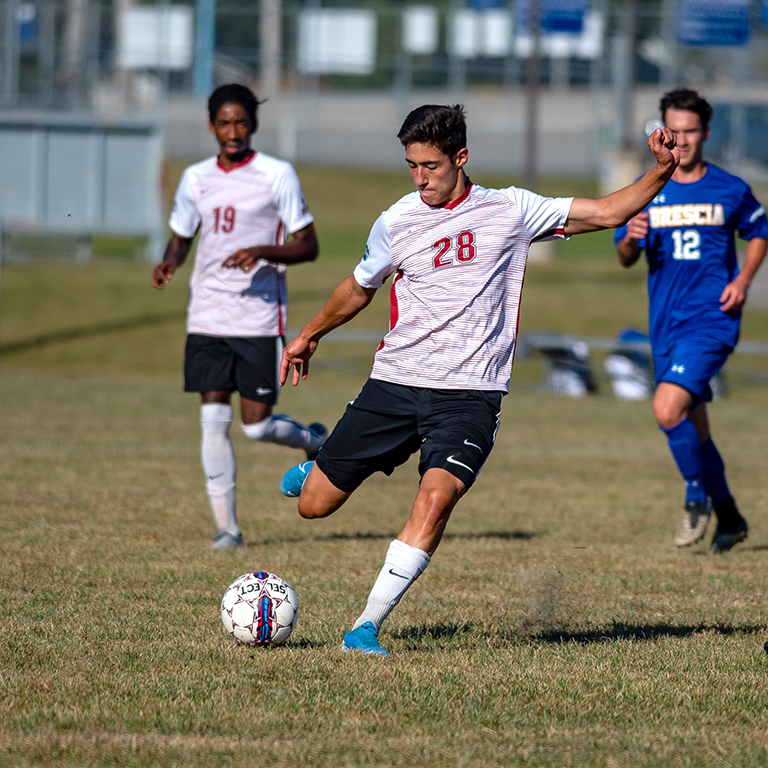 Three students playing soccer on a field.