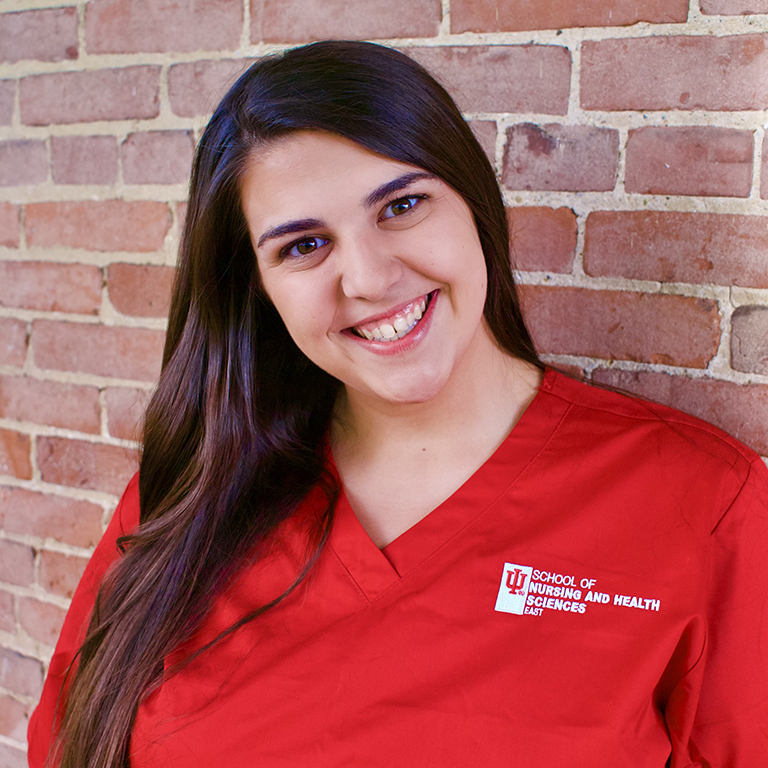 Close-up of Olivia Stottlemire in red scrubs in front of a brick wall