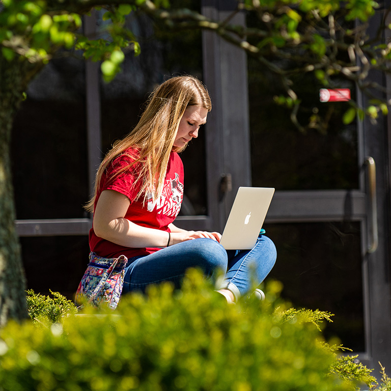IU East student sitting outside on a sunny day, working on her laptop