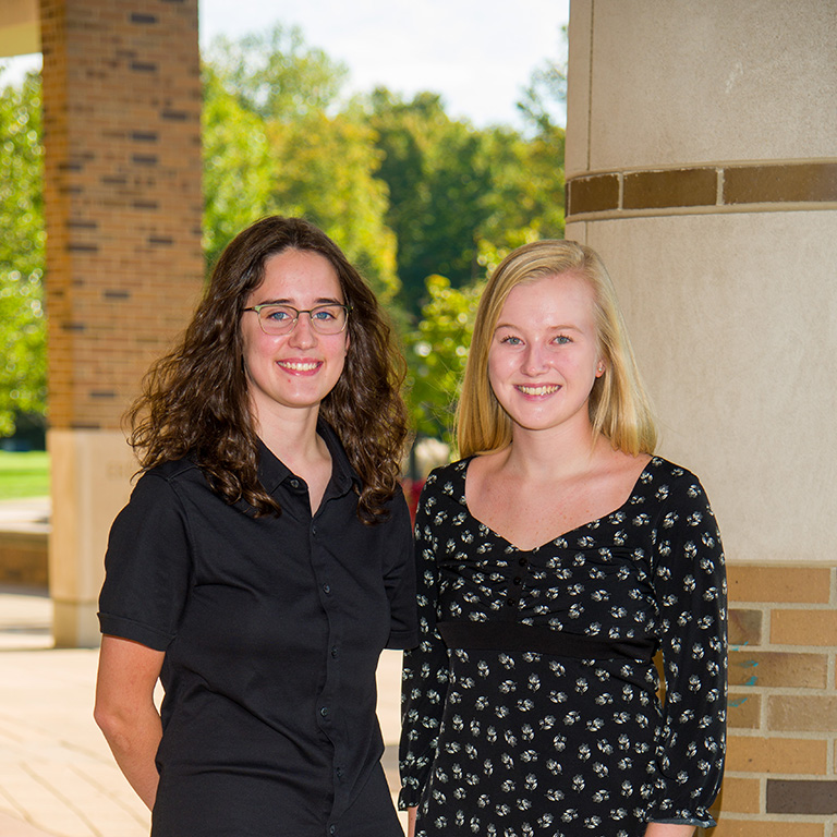 Jamie Andrews standing next to Alison Juday, outside, in front of a brick column.