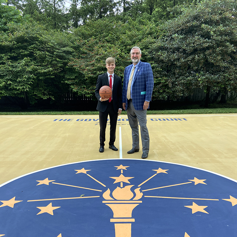Cole Fosbrink holding a basketball and standing beside Gov Holcomb on the state symbol