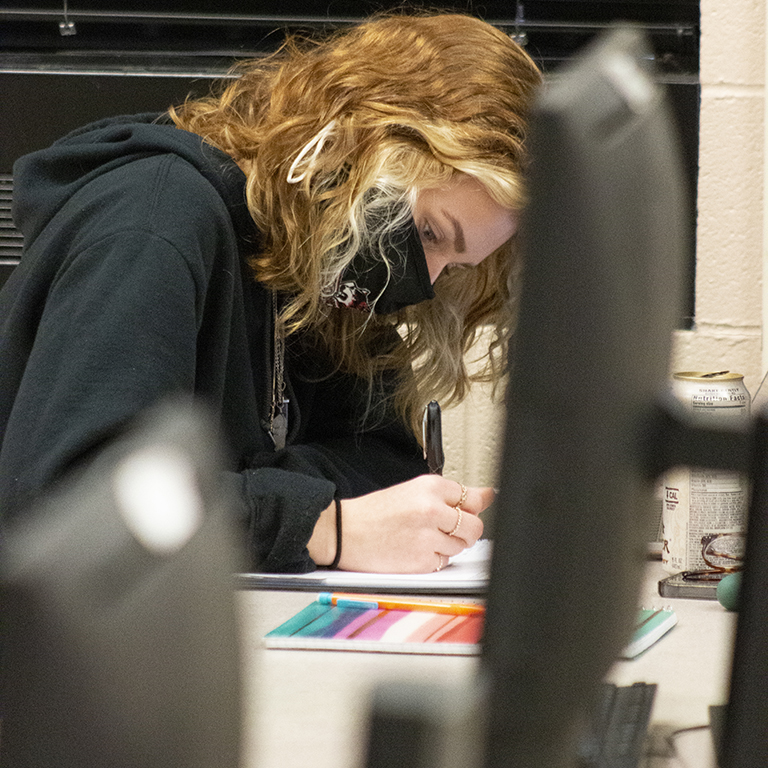 Delaney Hayes leaning over a table and writing in a notebook