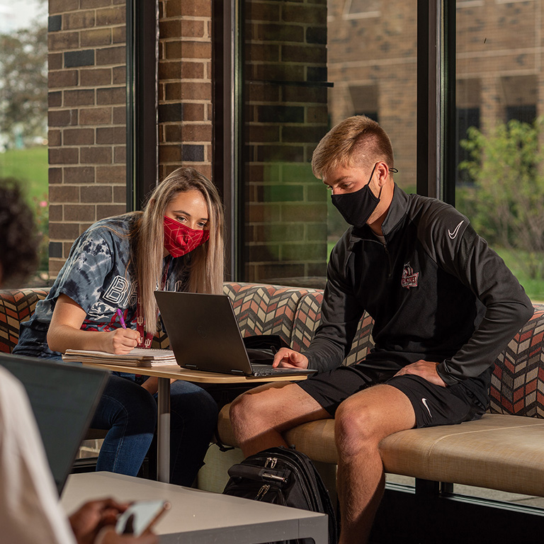 Student leans over to help another student at the center of the photo