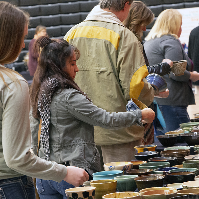 IU East Students participating at the Empty Bowls event. A line of participants look over a selection of unique ceramic bowls