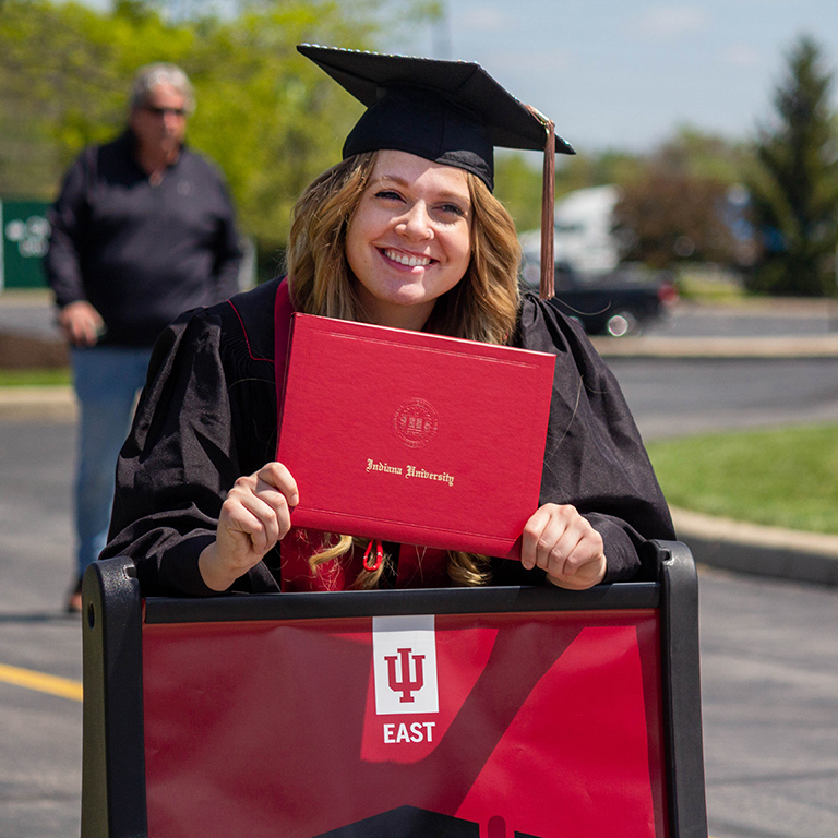 Graduate in cap, gown, and stole holding up their degree cover