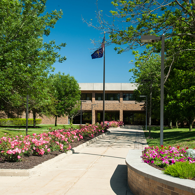 Whitewater Hall Rose Walkway, surrounded by flowerbeds and a flag pole leading up to the campus building
