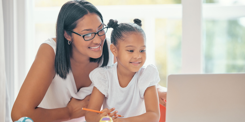 An adult female and female child holding a pencil look at laptop computer together.
