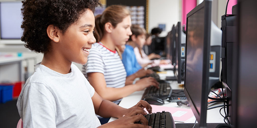 Youngsters sitting at desk working at computer keyboards and screens.