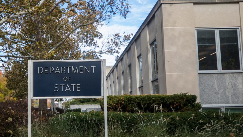 A black sign in front of a building that reads DEPARTMENT OF STATE