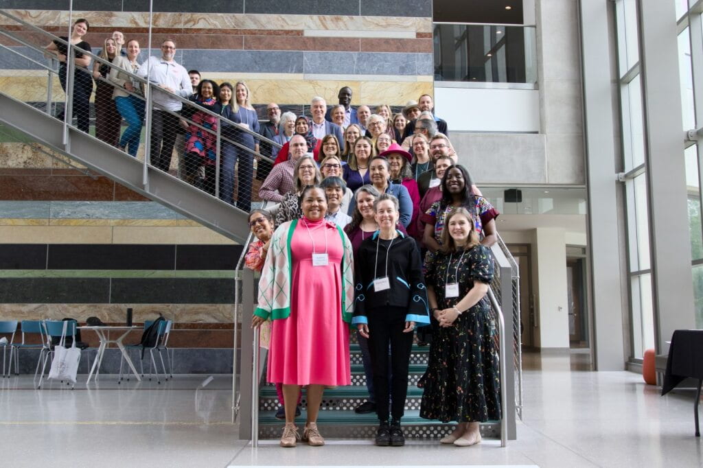 Rows of faculty fill a stairway. About thirty people pose for the camera.