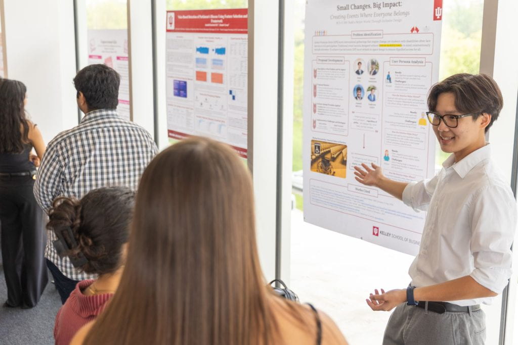 A student gestures to his research poster as he explains his project to onlookers.