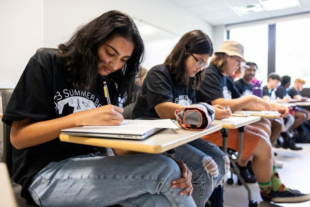 A theater viewed from the back. Rows of people sit listening to speaker Hilary Kahn who stands next to a large slide reading Global Learn...