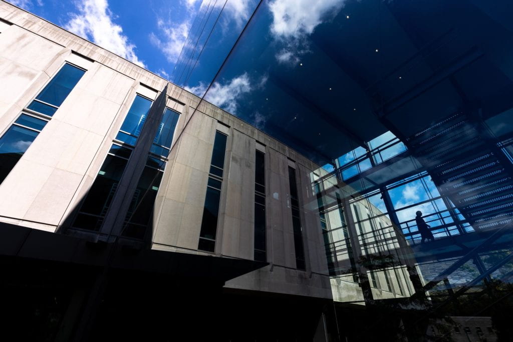 A limestone building is reflected in a floor-to-ceiling glass window. Through the
