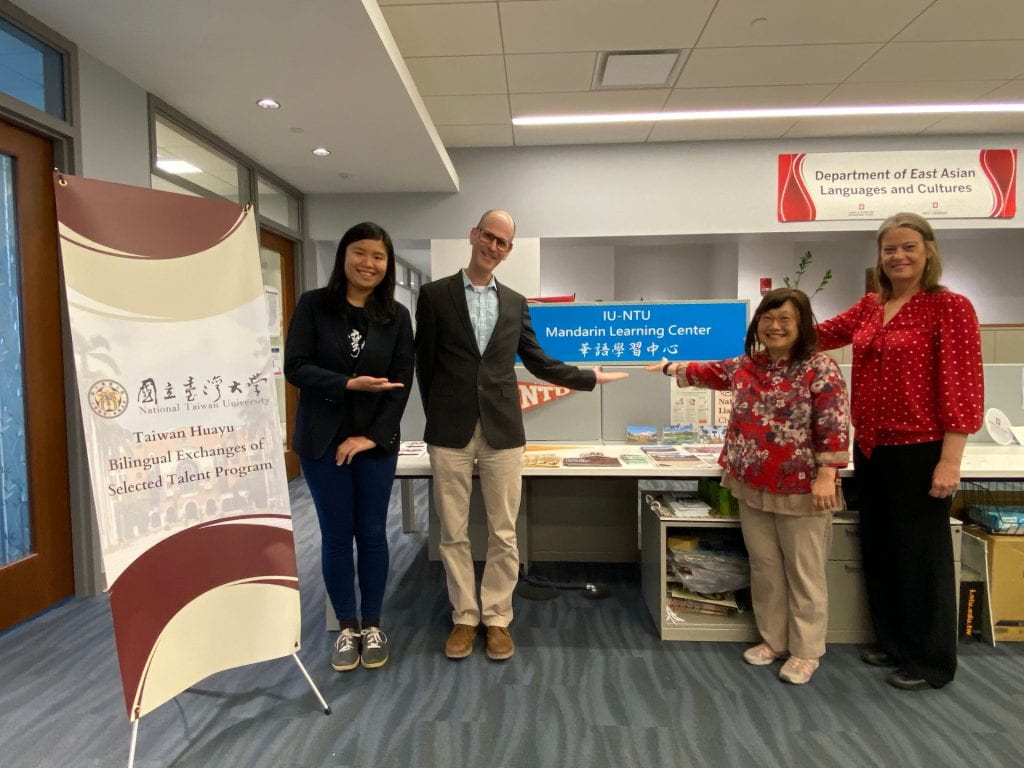 Three people stand gesturing to a sign.