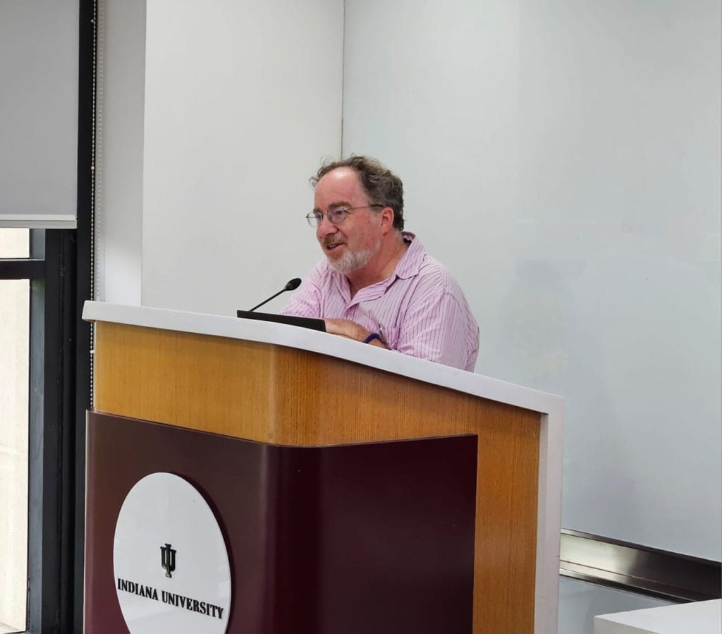 Alex Lichtenstein, a gray haired man with glasses, stands behind a podium at the IU India Gateway.