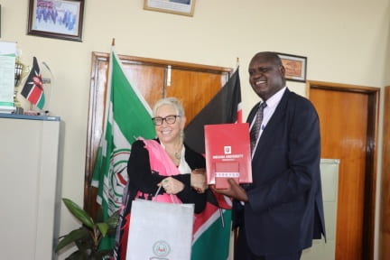Two people stand and exchange gifts, smiling at the camera