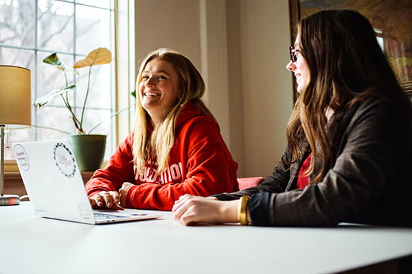 Two college-aged women work together at a laptop.