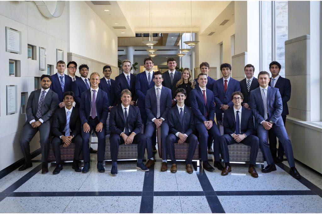 A group of twenty-one people in business attire posing in a spacious corridor with large windows and modern lighting.