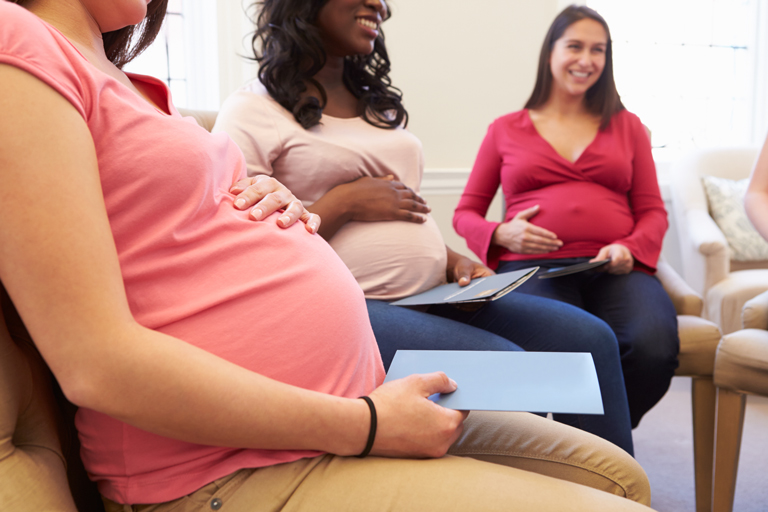 Two pregnant women seated with their hands on their bellies